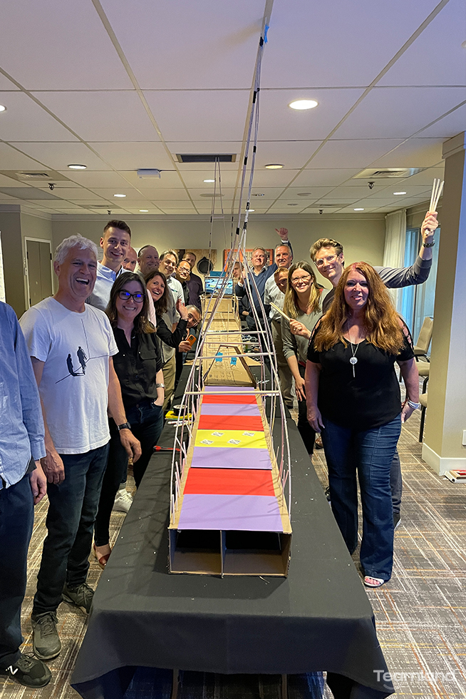 Corporate team building standing infront of a cardboard bridge build with Teamland logo